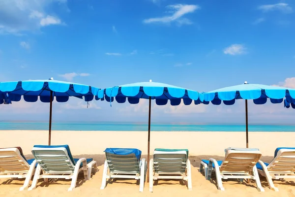 青いビーチ パラソルとラウンジャー砂浜の海岸に 休暇休日のバック グラウンドとビーチのコンセプト — ストック写真