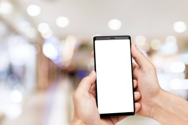 Adamın eli cep telefonuyla bulanık alışveriş merkezinin arka planında boş ekran.. 
