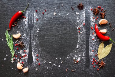 Koyu taş masada çeşitli otlar ve baharatlar var. Siyah masanın üzerinde tuz, baharat, biber, biberiye ve sarımsak var..