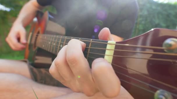 Człowiek siedzi w trawie i gra na gitarze. — Wideo stockowe