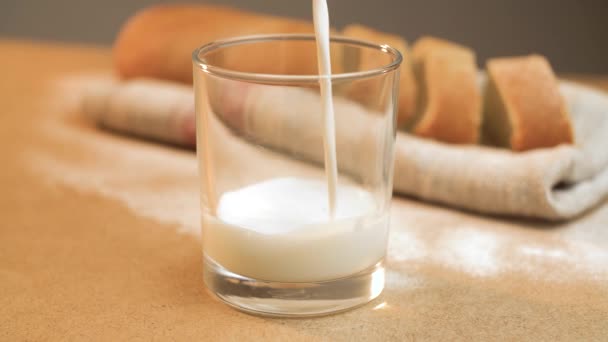 Tuangkan Susu Dalam Gelas Transparan Terhadap Latar Belakang Baguette Close — Stok Video