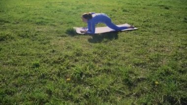 Eşofmanlı genç bir kız parkta halının üzerinde yoga yapıyor. Güneşli bir günde gün batımında temiz havada meditasyon kavramı..