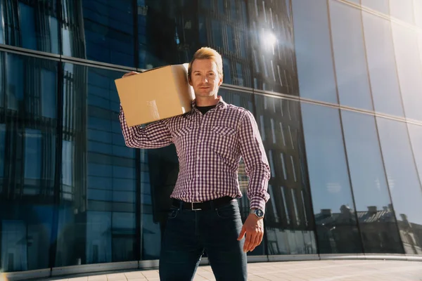 Joven hombre guapo en una camisa a cuadros sostiene una caja de papel . — Foto de Stock