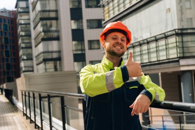Temiz bir inşaatçı samimi bir sevinç duygusu gösterir. Özel elbiseli ve kasklı bir adam. hazır bir iş merkezinin arka planına karşı