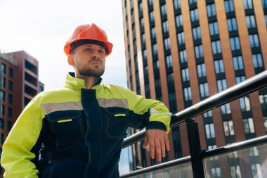 Temiz bir inşaatçı samimi öfke duyguları gösterir. Özel giysili ve kasklı bir adam, hazır iş merkezinin arka planına karşı düşmanlık gösteriyor.