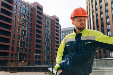 Temiz erkek müteahhit başka tarafa bakıyor. Özel elbiseli ve kasklı bir adam, bir iş merkezinin arka planına karşı planın ortasında bir ev inşa ederken görülüyor.