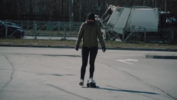 スケートボードに乗っている若い白人の女の子検疫ベルトの駐車場でコロナウイルス — ストック動画