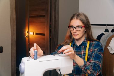 Küçük işletme terzileri, dairesinde giysiler, ev atölyesi. Kız dikiş makinesine iplik yerleştirir.