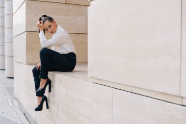 Yüksek topuklu ayakkabılı bir iş kadını çalışırken ofis binasının önünde oturur. Müdürün kontratı imzalamasını bekliyorum..
