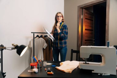 Bir atölyede dikiş ekipmanları ile kendinden emin bir terzi elinde tabletle müşterilerin ölçüsünü alıyor..