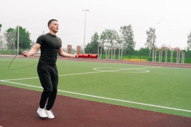 Genç bir erkek sporcu temiz havada ipin üzerinden atlıyor. Açık hava sporları konsepti