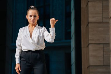 Sıra dışı geniş kaşlı şık kız elini yana doğru gösteriyor. Güzel giyimli iş kadını kaşlarını çatıyor..