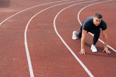 Koşucu koşmaya hazırlandı. Koşu koşucusu stadyumdaki koşu bandında oturuyor. Sporda atletizm kavramı.