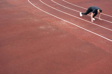 Koşucu koşmaya hazırlandı. Koşu koşucusu stadyumdaki koşu bandında oturuyor. Sporda atletizm kavramı.