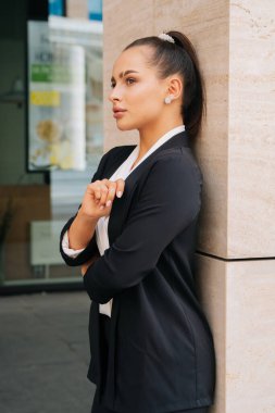 Düşüncelere dalmış şık bir kız takım elbisesiyle yana bakıyor. İş merkezinin arka planına karşı ortalama bir plan.