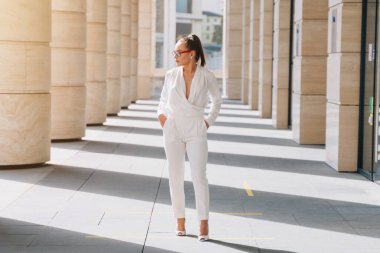 Beyaz pahalı takım elbiseli, güzel gözlükleri olan şık bir kız. Kavkah modeli Fotoğrafçı için poz veriyor.