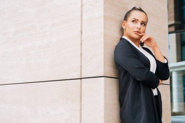 Zarif, şık bir bayan siyah bir takım elbiseyle bir iş merkezinin duvarına yaslanıyor. Kız zevkle gözlerini kapattı..