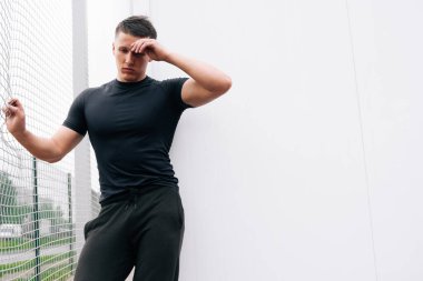 Düşünceli, yakışıklı bir fitness eğitmeninin portresi. Futbol sahasındaki atletik genç adam..