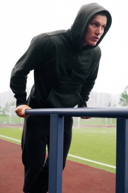 Bir adam caddeye yanaşıyor. Beden eğitimi eğitmeni çubuklardaki simülatöre basar. Açık hava sporları konsepti.