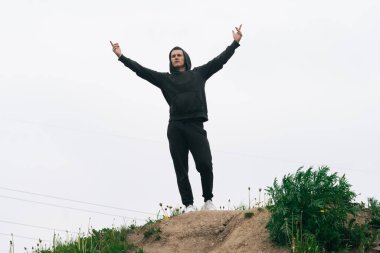 Siyah eşofmanlı bir adam elleri havada dağlarda duruyor. Sabahları açık hava sporları konsepti.