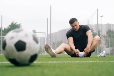 Futbolcu. Adam ayağını tutuyor. Futbol topuna odaklan. Eklem yerinden çıkmış ya da burkulmuş. Spor yaparken düşme konsepti. Eğitimde bacağını kır.