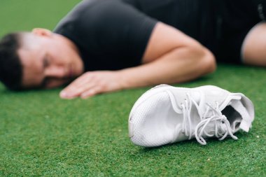 Bir futbol sahasının çimlerine düşen bir adamın yakın plan fotoğrafı. Spor ayakkabılarına odaklan. Eğitim sırasında ağır yaralanma kavramı.