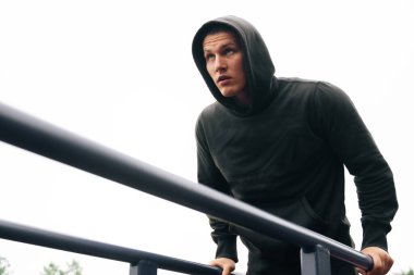 Genç sporcu fitness antrenörü stadyumdaki oyun alanında triseps kasları için egzersiz yapıyor. Vücut geliştirici sokak fitness ekipmanları üzerine eğitim alıyor, geri dön.