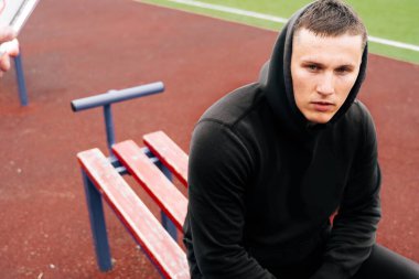 Genç bir Avrupalı vücut geliştiricinin portresi bir bankta yan yana oturuyor. Sokak simülatörü kullanarak eğitim. Çocuk parkındaki adama yaklaş.