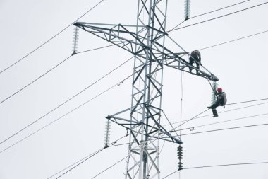 Erkek elektrikçiler elektrik kulesinde tamirat yapıyor. Elektrik hattı gökyüzüne karşı. Elektrikçi çalışma konsepti