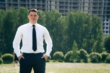 Bina inşaatının arka planında beyaz gömlekli dalgın bir adamın portresi. Doğanın mavi gökyüzüne sahip bir vincin arka planındaki akıllı mühendis kavramı..