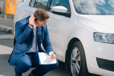 Adamın biri arabanın yanındaki tablete yazıyor. Yolda bir kaza oldu, hava yastığı çalışmadı. Kaza, genç bir adama zarar verdi. Kazadan sonra arabayı sigortala.