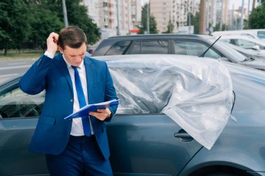 Adamın biri arabanın yanındaki tablete yazıyor. Yolda bir kaza oldu, hava yastığı çalışmadı. Kaza, genç bir adama zarar verdi. Kazadan sonra arabayı sigortala.