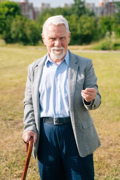 Stylish old man asks to give money. Portrait of a long old merry European grandfather in nature.