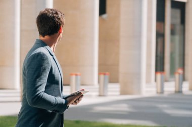 Genç bir adam şık bir iş elbisesi içinde bir gökdelenin arka planında dijital tabletle yan tarafa döndü.