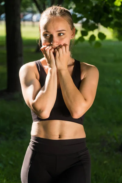 フィットネス選手の若い怖がっている女の子は顔に手を保持します 公園での屋外トレーニング中の驚きの概念 — ストック写真