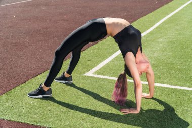 Güzel bir kızla spor yapmak, bir yaz günü stadyumda köprü oluşturur. Formda olan şık giyimli genç bir kadın için yaygın bir plan.