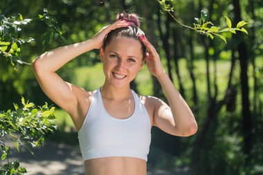 Parkta genç ve güzel bir kızın portresi spor beyaz bir bluzla toplanmış saçlarıyla, kadınlar arkalarından tek başlarına dolaşırlar.