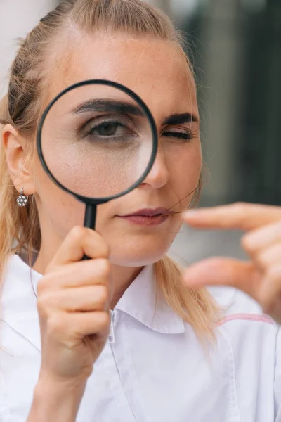 虫眼鏡をかけ小さなサイズを見せる医師の女性の肖像画 医者は検査のために虫眼鏡を調べる — ストック写真