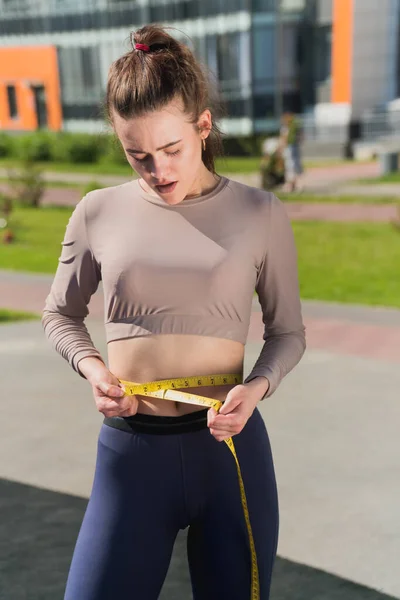 細い女の子は手にセンチのテープを持ってる 公園内の不適切な減量女性フィットネストレーナーの概念 — ストック写真