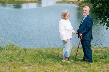 Gölün arka planında ayakta duran neşeli, beyaz, yaşlı bir adam ve kadının portresi. Parlak bir gelecek arayan mutlu büyükanne ve büyükbaba kavramı