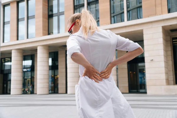 Eine Frau Weißer Medizinischer Kleidung Hält Sich Ihrem Rücken Fest lizenzfreie Stockfotos