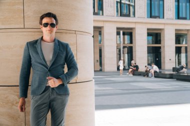 Şehrin arka planında güneş gözlüklü şık bir genç adam. İnşaat mühendisi kavramı çok katlı bir binanın yakınında.