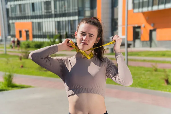 面白いいたずら娘は手にセンチメートルのテープを持っています 公園内の不適切な減量女性フィットネストレーナーの概念 — ストック写真