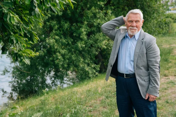 A brooding stylish old man in a business suit against the background of the forest. Grandpa spread his arms aside from surprise