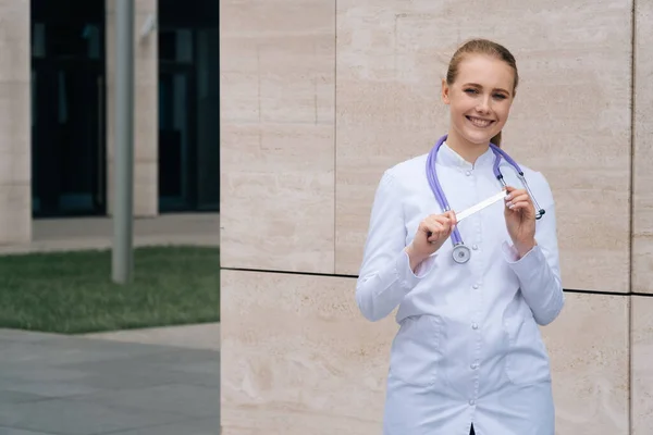 Een mooi meisje met een glimlach in een medisch gewaad houdt een metalen spatel vast — Stockfoto