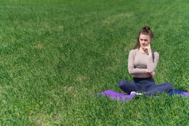 Üzgün, düşünceli bir kız yoga ceketi giyer, temiz havada aynı şekilde dinlenir, telefonla konuşur, akıllı telefonu arar, sosyal uzaklık...
