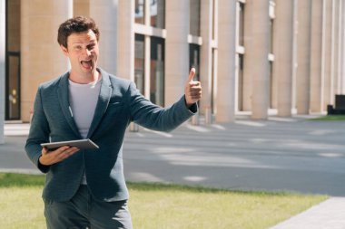 Takım elbiseli şık bir genç adam elini yüzüne bir iş merkezinin arka planına dayadı.