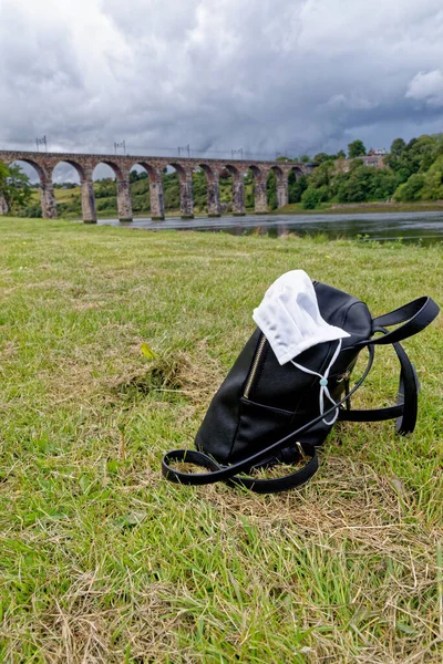 Travel in pandemic time - medical mask and backpack with Royal Border Bridge in background. Berwick-upon-Tweed, Northumberland, England - 23rd of July, 2020
