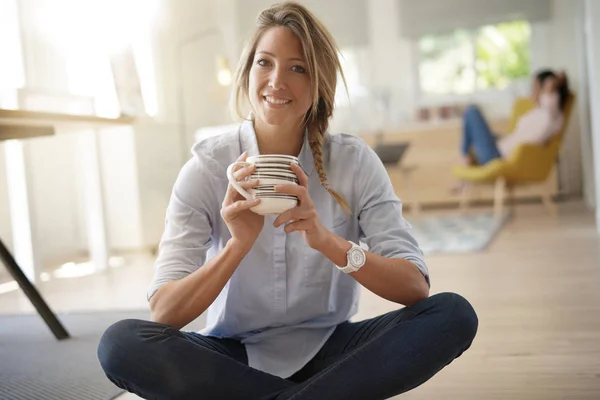 Beautiful 30-year-old woman drinking hot tea, sitted on floor