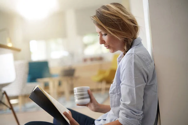 Beautiful 30-year-old woman relaxing with book and hot tea